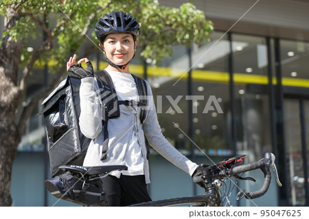 A food delivery delivery woman carrying a delivery bag in front of a road bike and signing OK 95047625