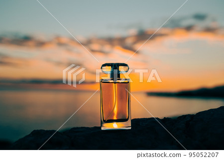 A glass bottle of luxury perfume on the ocean. Sunset in the background. Close-up low angle view. Presentation of cosmetic products 95052207