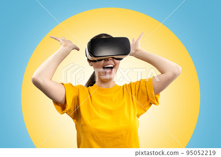 A young happy woman in virtual reality glasses, in amazement, stretches out her hands in different directions. Blue background with a yellow circle. The concept of virtual reality 95052219