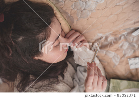 sick girl in bed looking at thermometer sick girl in bed looking at thermometer 95052371