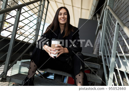 portrait of a successful business woman with a cup of coffee and a wide smile sitting on the stairs portrait of a successful business woman with a cup of coffee and a wide smile sitting on the stairs 95052660