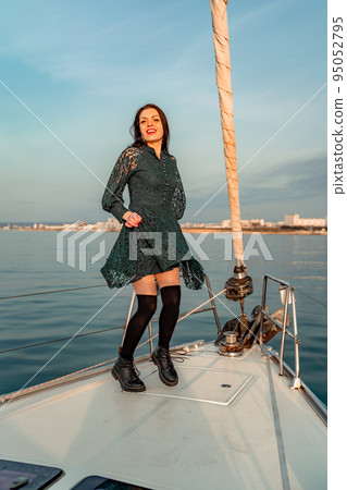 Woman standing on the nose of the yacht at a sunny summer day, breeze developing hair, beautiful sea on background 95052795