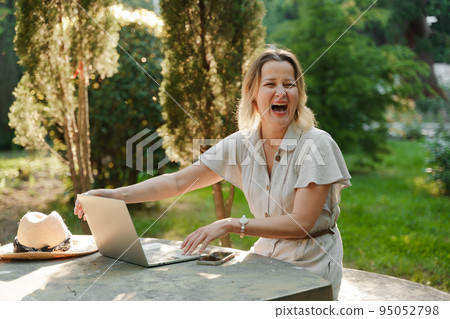 a beautiful mature woman in glasses works on a computer at a white table in nature and spends her day productively 95052798