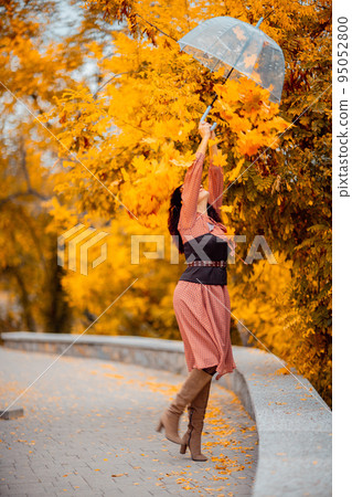 Beautiful girl in a dress with an umbrella in the autumn park. She holds him over her head, autumn leaves are falling out of him 95052800