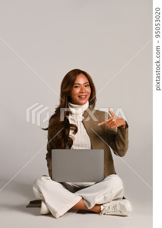 Smiling young woman sitting with laptop on white background. Studio photo, people and technology concept Smiling young woman sitting with laptop on white background. Studio photo, people and technology concept 95053020