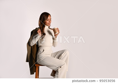 Beautiful fashionable woman holding paper cup sitting on white background. Autumn fashion and beauty concept 95053056