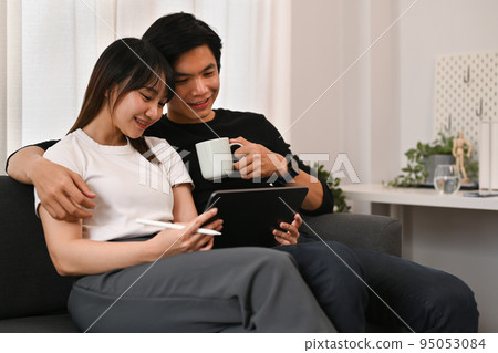 Young asian couple enjoying spending time together at home and surfing internet on digital tablet. People and technology concept 95053084