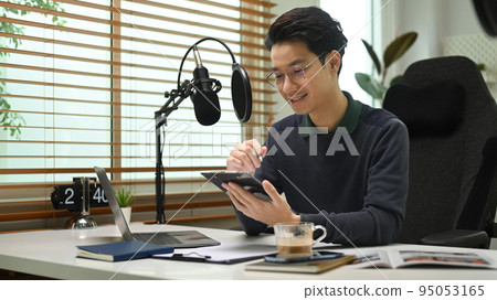 Young man podcaster speaking into a condenser microphone, recording podcast from home studio 95053165