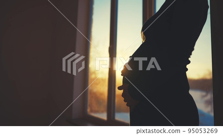 pregnant woman. motherhood a pregnancy light concept. 40 year old pregnant woman stands in a dress by the window holding her stomach silhouette. silhouette of a girl in at sunset by the window pregnant woman. motherhood a pregnancy light concept. 40 year old pregnant woman stands in a dress by the window holding her stomach silhouette. silhouette of a girl in at sunset by the window 95053269
