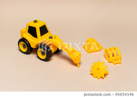 Children's plastic toy on a beige background - a yellow tractor with different nozzles drill, saw on wood, a wood loader, a bucket excavator. Construction equipment for children. 95054146