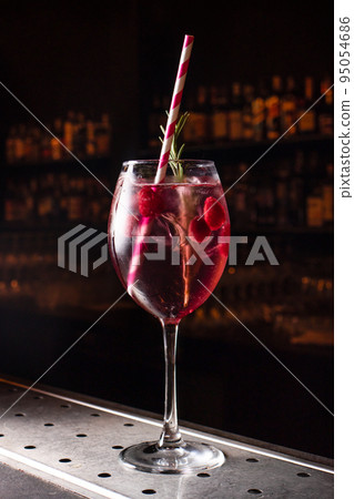 Raspberry cocktail with ice and a tube in a glass on a black background on the bar. Bright colorful berry cocktail with alcohol 95054686