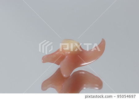 Plastic artificial false unit tooth. Dental prosthesis close-up on a blue background. Dentistry conceptual photo. Prosthetic dentistry. False teeth 95054697