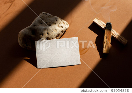 Still life scene with hard shadows on brown background in sunlight glass and blank business, greeting card, invitation mockup. Long harsh shadows. New naturalism Still life scene with hard shadows on brown background in sunlight glass and blank business, greeting card, invitation mockup. Long harsh shadows. New naturalism 95054858