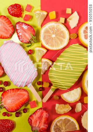 Two ice creams on a sticks - strawberry and lemon on a yellow and red background. Summer fruit desserts. Two ice creams on a sticks - strawberry and lemon on a yellow and red background. Summer fruit desserts. 95055058