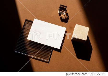 Still life scene with hard shadows on brown background in sunlight glass and blank business, greeting card, invitation mockup. Long harsh shadows. New naturalism Still life scene with hard shadows on brown background in sunlight glass and blank business, greeting card, invitation mockup. Long harsh shadows. New naturalism 95055118