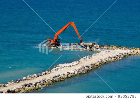 An excavator and a mining truck move stones into the sea. Construction of breakwaters to protect the beach in Netanya in Israel. 95055785