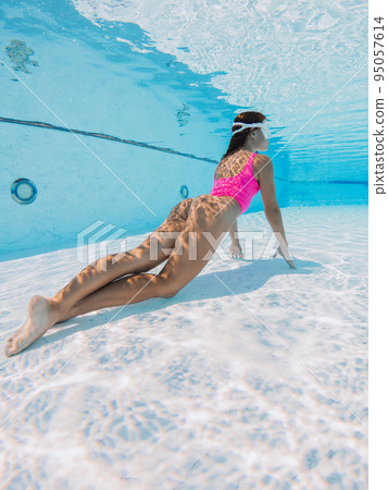 Attractive woman with pink swimsuit posing underwater in pool Attractive woman with pink swimsuit posing underwater in pool 95057614