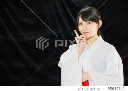 A Japanese woman in shrine maiden clothes pointing to the blank space on a black background 95059641