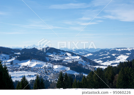 OBERSTAUFEN, GERMANY - 29 DEC, 2017: Wonderful view of the snow-covered winter sports resort of Oberstaufen in the Bavarian Alps with green coniferous trees in the foreground 95060226