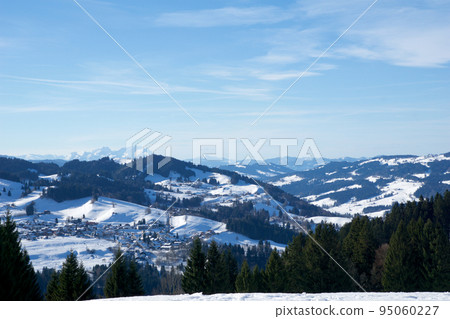 OBERSTAUFEN, GERMANY - 29 DEC, 2017: Wonderful view of the snow-covered winter sports resort of Oberstaufen in the Bavarian Alps with green coniferous trees in the foreground 95060227