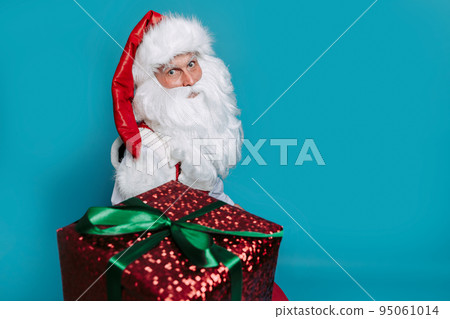 Santa Claus gives xmas gift box while looking at camera on blue studio background. New Year concept Santa Claus gives xmas gift box while looking at camera on blue studio background. New Year concept 95061014