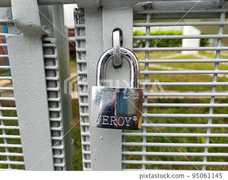 JOHOR, MALAYSIA -AUGUST 1, 2022: Stainless steel pad lock is used to lock the gate. A rust-resistant type of pad lock is used for fences that are exposed to the weather. 95061145