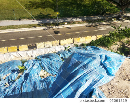 MELAKA, MALAYSIA - JULY 6, 2022: Slopes that have been cut, are temporarily covered using plastic or fabric for a while to prevent erosion caused by rainwater. This is as an immediate action. 95061819