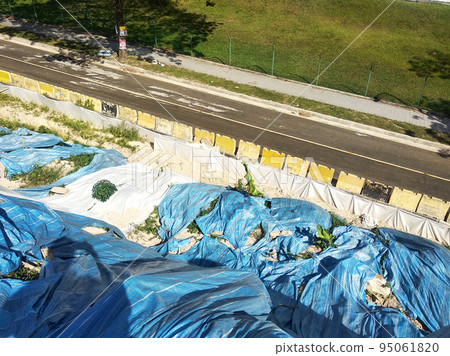 MELAKA, MALAYSIA - JULY 6, 2022: Slopes that have been cut, are temporarily covered using plastic or fabric for a while to prevent erosion caused by rainwater. This is as an immediate action. 95061820