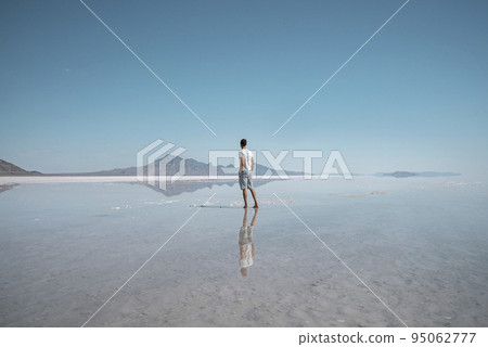 Man sightseeing Bonneville salt flat and mountains. Tourist exploring beautiful peak reflecting in water with clear sky in background. He is spending leisure time during summer vacation. Man sightseeing Bonneville salt flat and mountains. Tourist exploring beautiful peak reflecting in water with clear sky in background. He is spending leisure time during summer vacation. 95062777