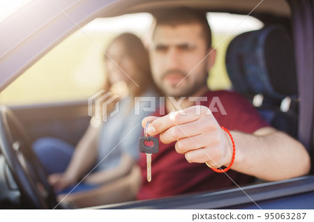 Male and woman in car, focuse on keys. Blurred background. Man holds keys from vehicle, sells his automobile, advertises auto. Horizontal shot of young successful driver and his female companion 95063287