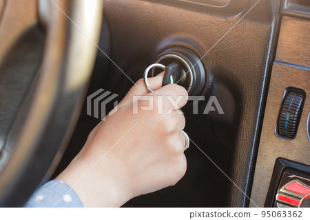 Woman`s hand on car`s key, tries to start engine, turn on key in keyhole, auto`s panel and wheel in background. Key inserted in lock. Beginning journey. Starting car concept Woman`s hand on car`s key, tries to start engine, turn on key in keyhole, auto`s panel and wheel in background. Key inserted in lock. Beginning journey. Starting car concept 95063362