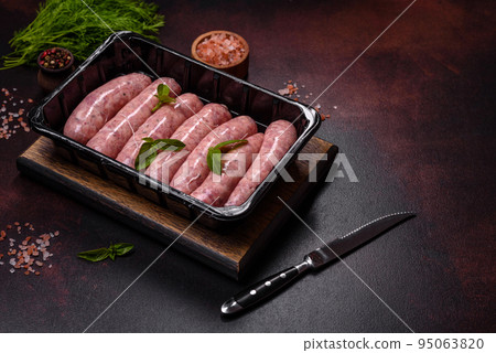 Raw sausages with ingredients on a cutting board on a dark concrete background with copy space Raw sausages with ingredients on a cutting board on a dark concrete background with copy space 95063820