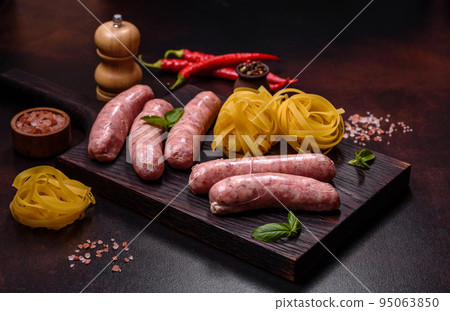 Raw sausages with ingredients on a cutting board on a dark concrete background with copy space Raw sausages with ingredients on a cutting board on a dark concrete background with copy space 95063850