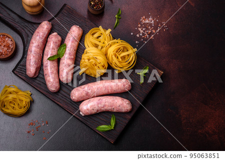 Raw sausages with ingredients on a cutting board on a dark concrete background with copy space 95063851