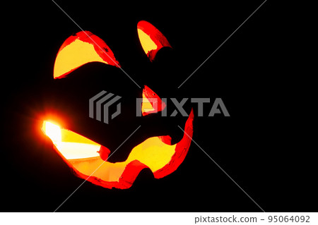 The face of a candlelit jack-o'-lantern in the dark 95064092