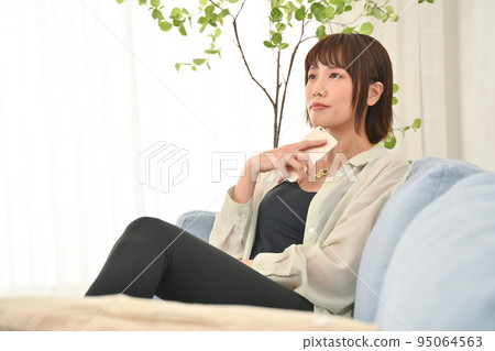 A woman sitting on a sofa and using a smartphone A woman sitting on a sofa and using a smartphone 95064563