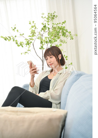 A woman sitting on a sofa and using a smartphone A woman sitting on a sofa and using a smartphone 95064564
