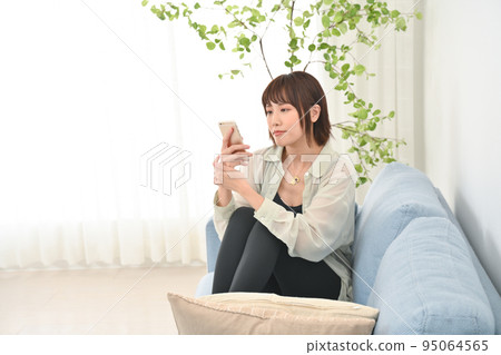 A woman sitting on a sofa and using a smartphone A woman sitting on a sofa and using a smartphone 95064565