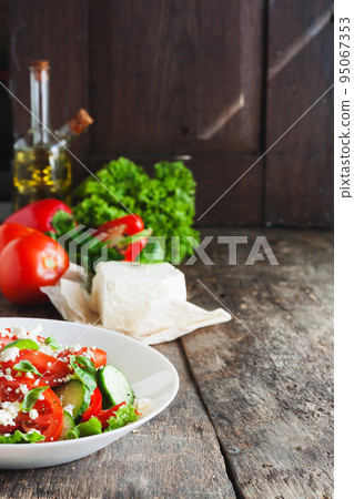 Shopska salad in a white plate on a wooden background, a number of raw ingredients lettuce. 95067353