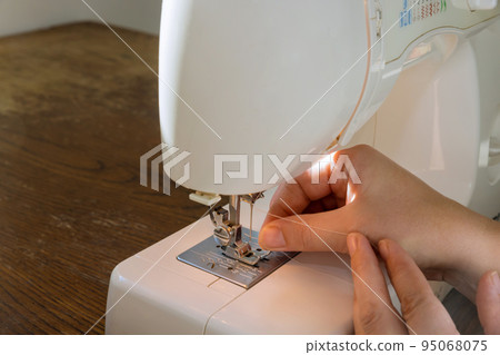 Sewing machine needle hole with thread pulled into it by the hand of the seamstress Sewing machine needle hole with thread pulled into it by the hand of the seamstress 95068075