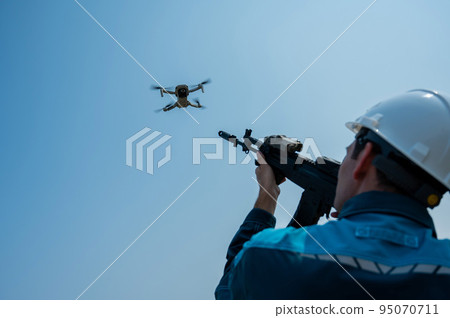 Caucasian man in a helmet shoots a flying drone with a rifle.  95070711