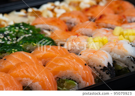 Sushi rolls background in package after delivery. Philadelphia roll in sushi set close up. Traditional Japanese food. Japanese kitchen with sea food. Taking one sushi roll from set using chopsticks 95070923