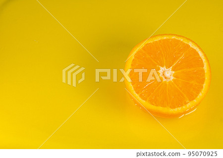 Water falling from orange hue orange on yellow background. Orange slice and water splashing, drops of juice falling from juicy fruit. Making cocktail of fruits, drinking cold lemonade 95070925