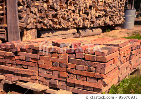 Red brick packed in stack are stored on ground outdoors at a hardware store warehouse. Building bricks on pallet on an outdoor warehouse 95070933