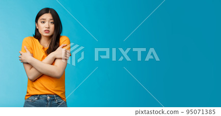 Girl feeling uncomfortable walking light yellow t-shirt, hugging herself trembling, shaking feeling cold, freezing windy weather, frowning grimacing discomfort, stand blue background 95071385