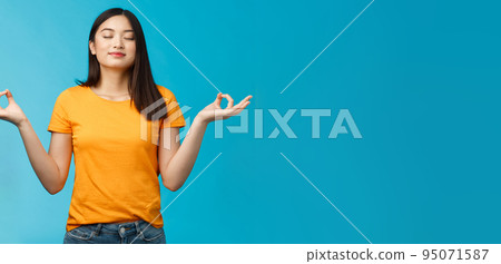 Peaceful charming relaxed asian girl buddhist meditating, breathing, inhale fresh air practice yoga, close eyes smiling relieved, stand lotus nirvana pose, reach zen, standing blue background 95071587