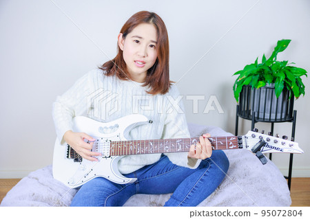 Woman playing guitar indoors, hobby, lessons, entertainer Woman playing guitar indoors, hobby, lessons, entertainer 95072804
