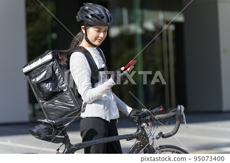 一個送餐的女人,手裡拿著智能手機,拉著一輛公路自行車 一個送餐的女人,手裡拿著智能手機,拉著一輛公路自行車 95073400