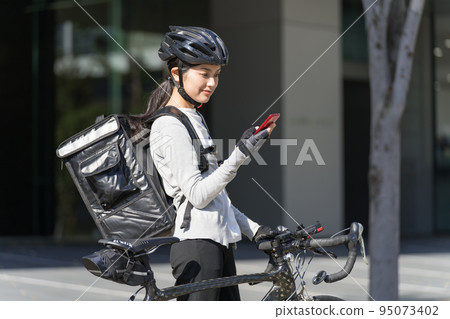 一個送餐的女人，手裡拿著智能手機，拉著一輛公路自行車 95073402