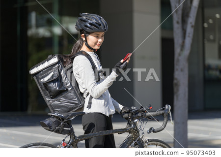 一個送餐的女人，手裡拿著智能手機，拉著一輛公路自行車 95073403